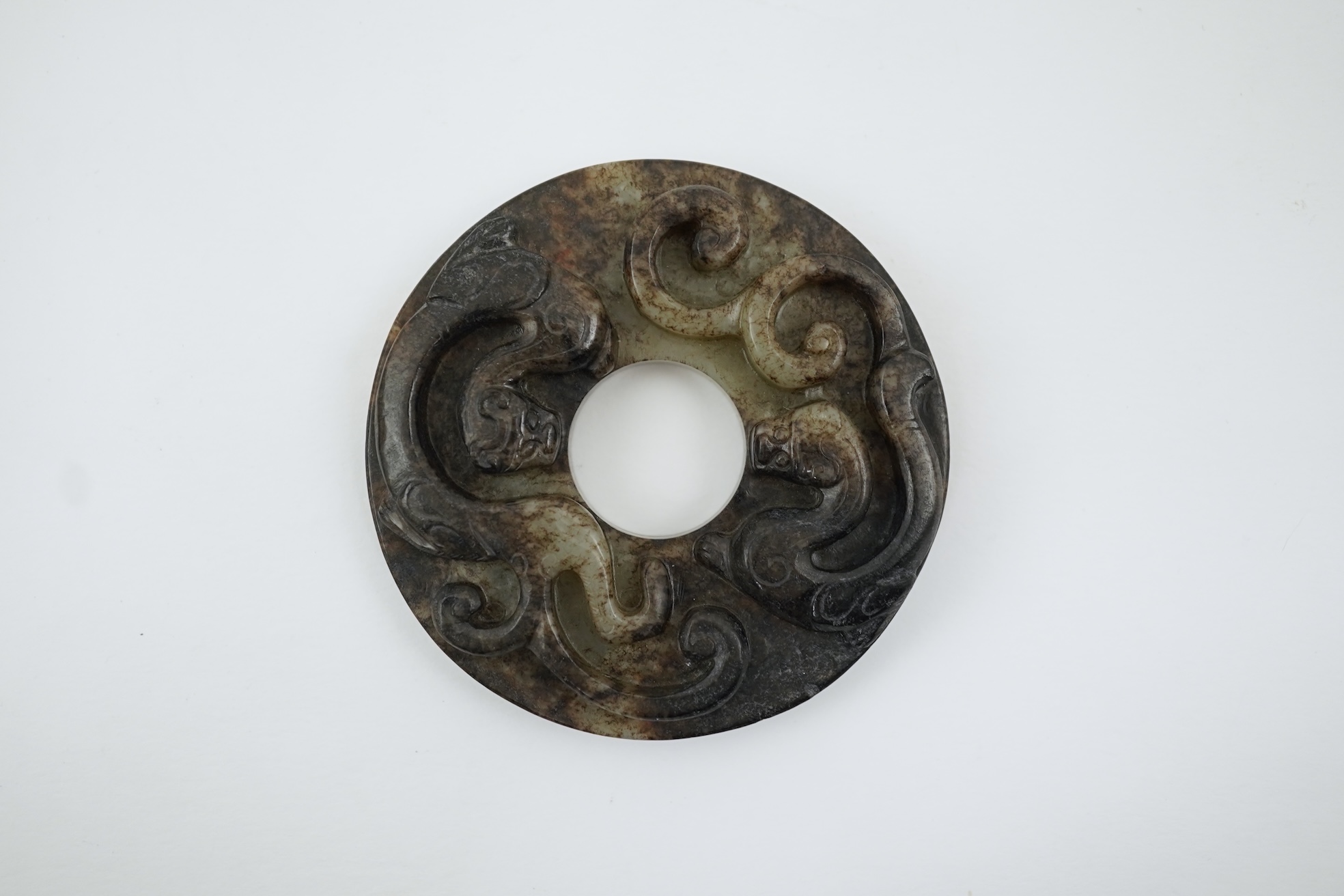 A Chinese pale celadon and black jade bi disc